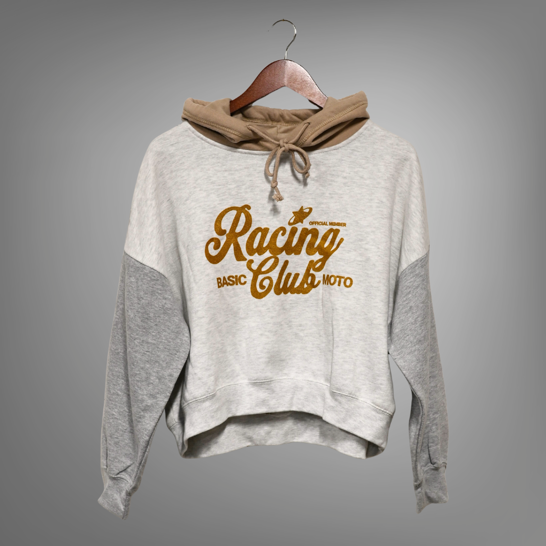 Multi color crop hoodie with gold text on a hanger against a gray background